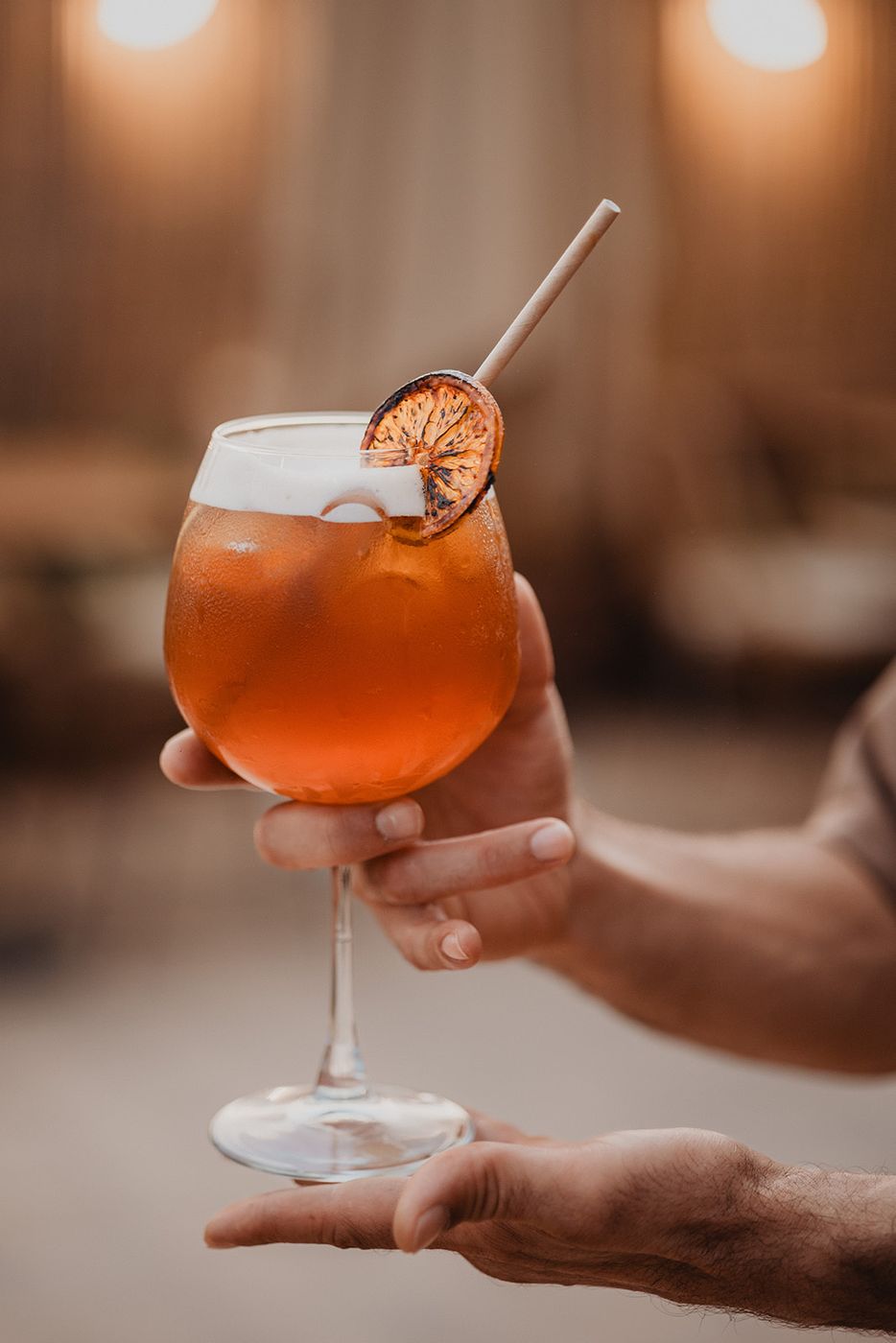 Amber drink held by a waiter, dried orange